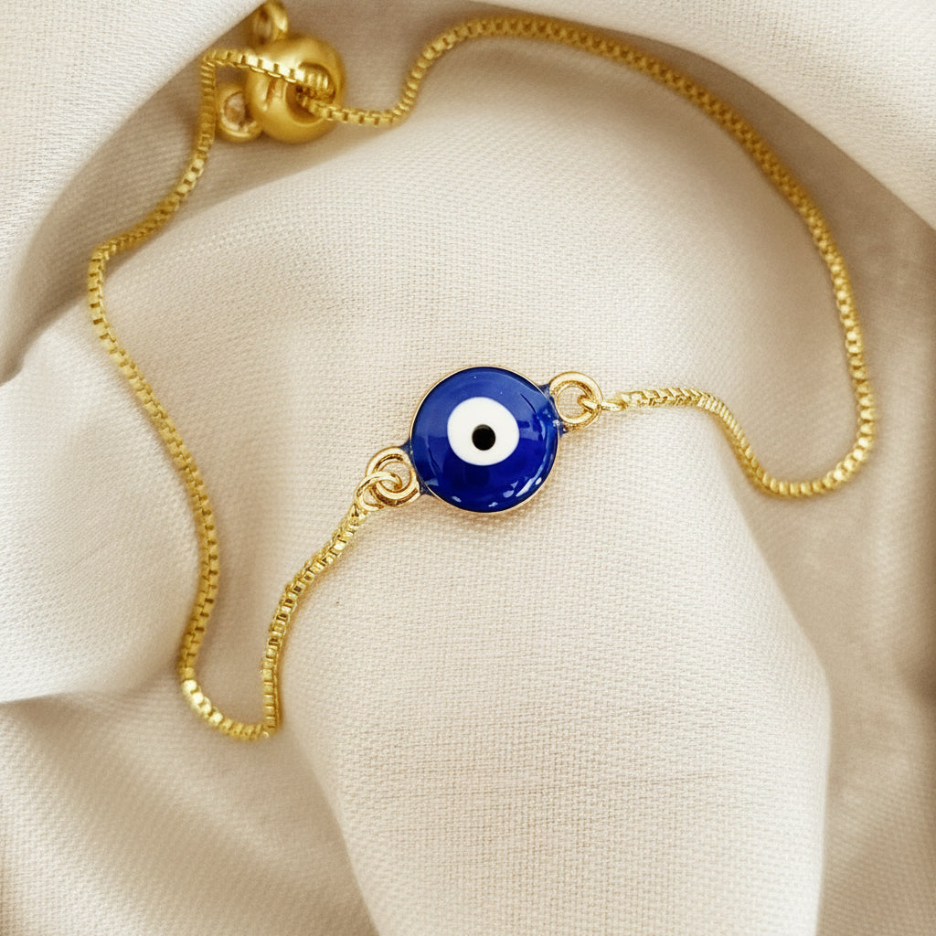 Gold bracelet with a blue evil eye charm on a white surface