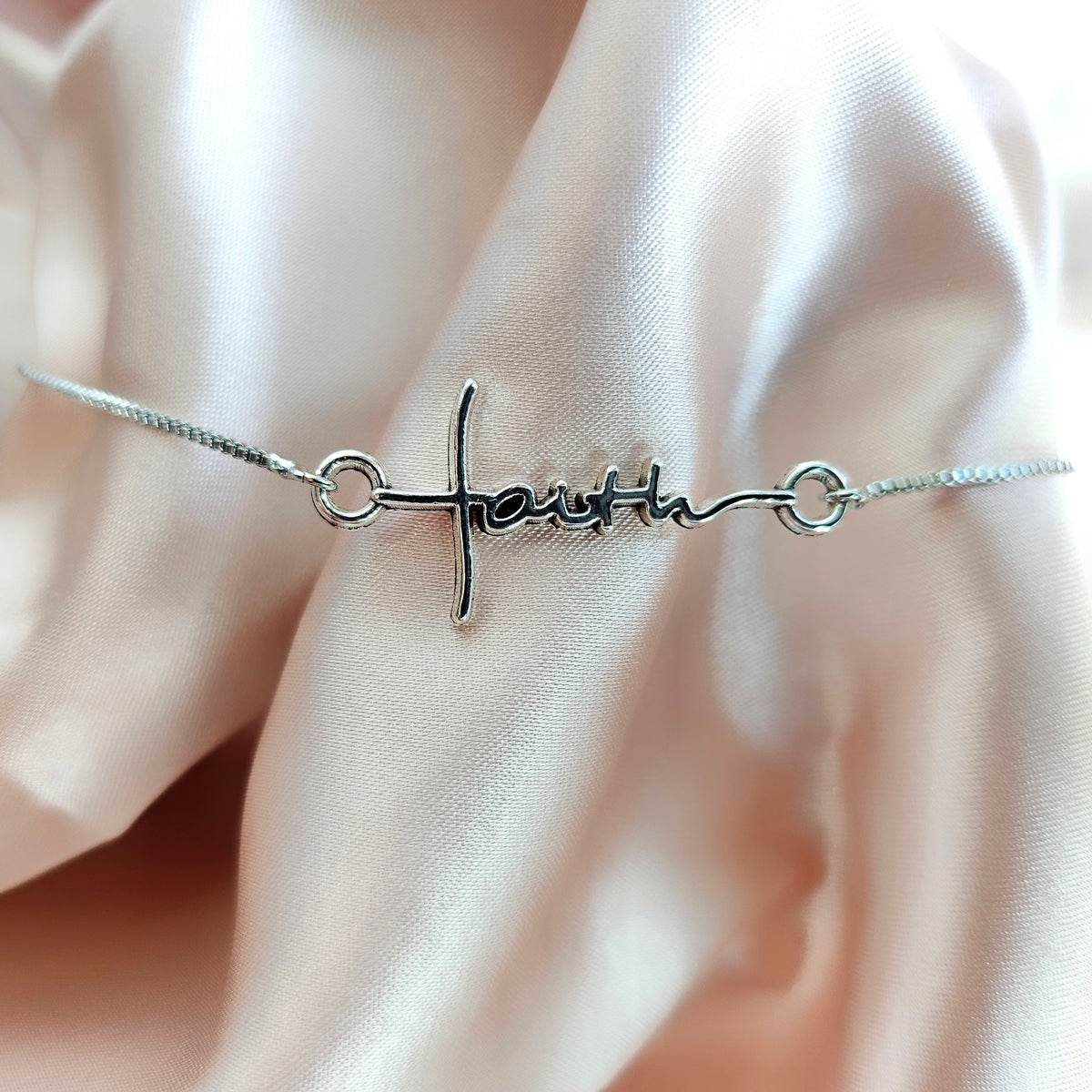 Silver bracelet with &#39;faith&#39; on a soft pink fabric background