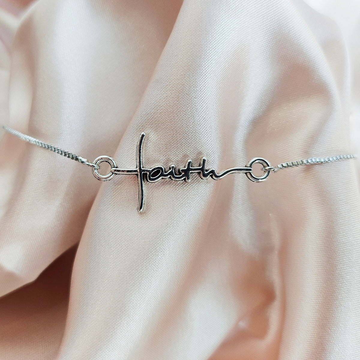 Silver bracelet with &#39;faith&#39; on a soft pink fabric background