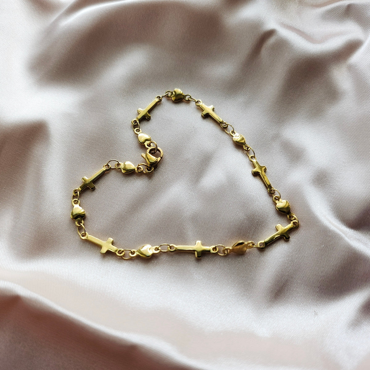 Gold bracelet with heart and cross designs on a soft fabric background