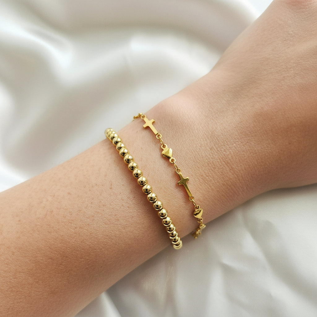 Gold bracelet with beads and crosses on a wrist against a white background