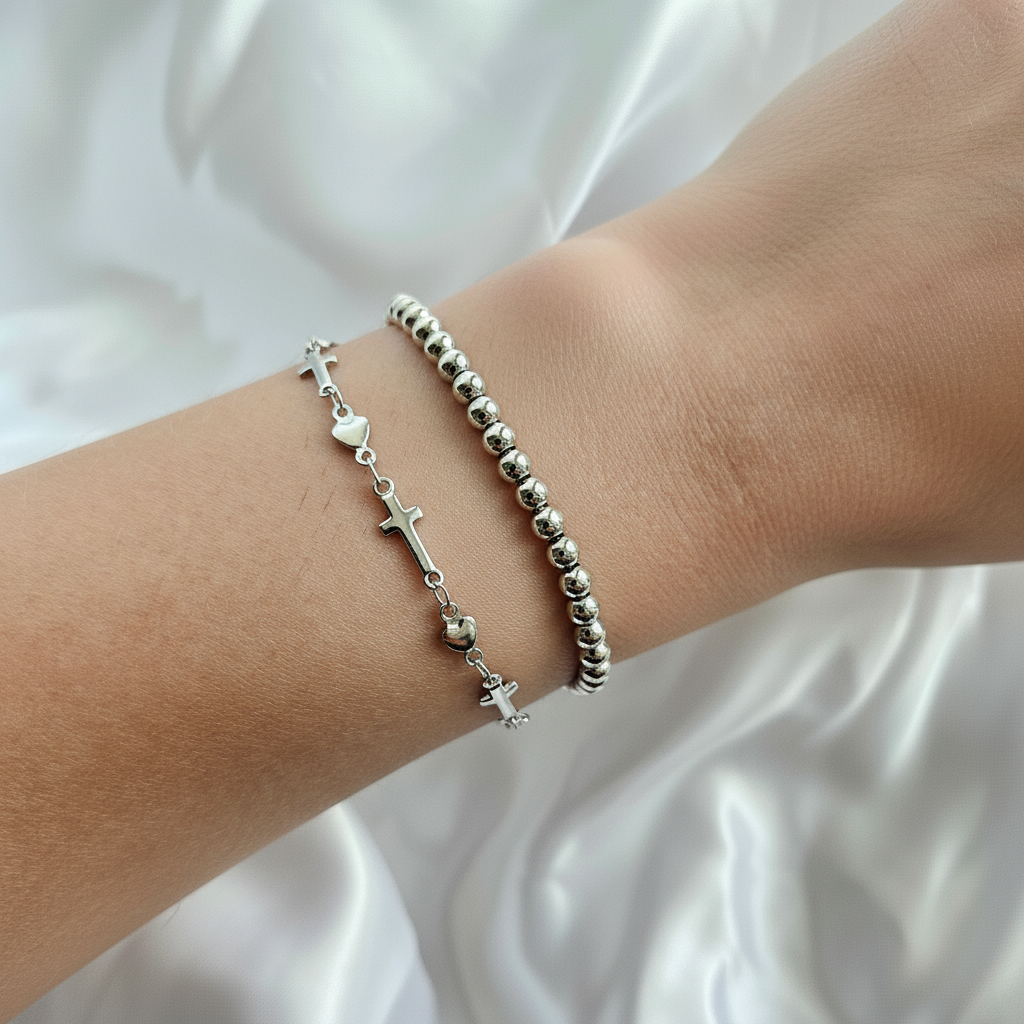 Silver bracelet with heart and cross charms on a wrist against a white fabric background