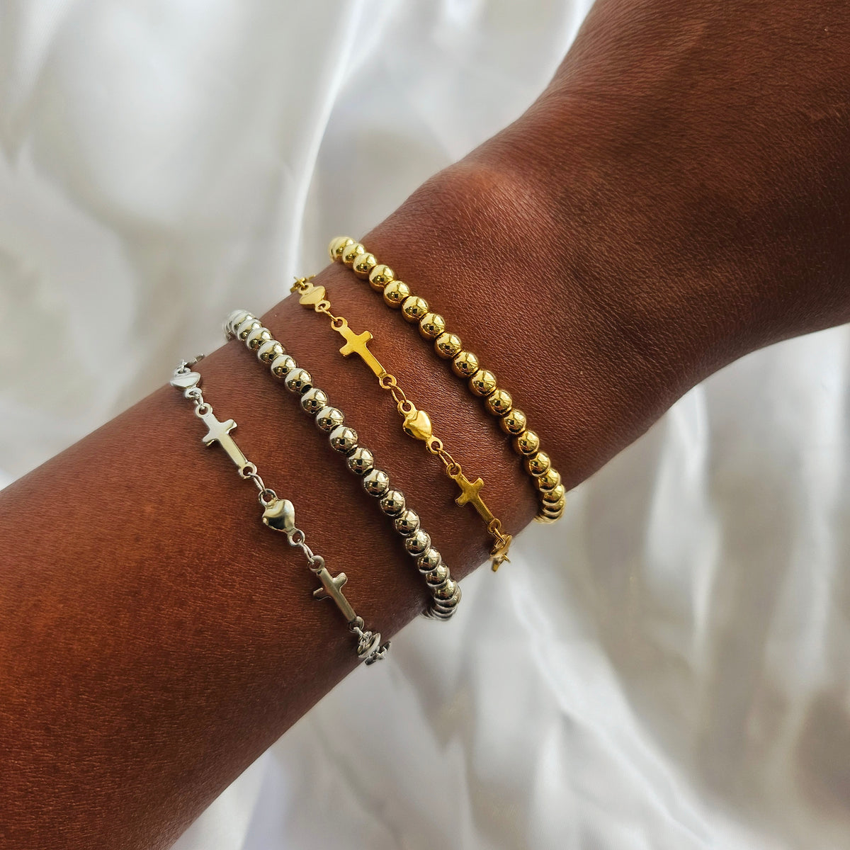 Bracelets with crosses and heart charms on a wrist against a white background